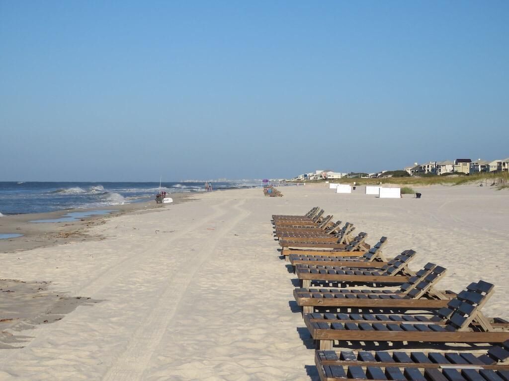 A beach with rows of wooden sun loungers facing the ocean.