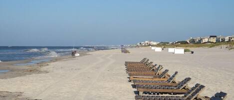 A beach with rows of wooden sun loungers facing the ocean.
