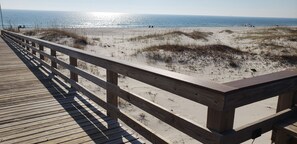 Ein hölzerner Steg führt zu einem Strand mit Dünen und dem Meer im Hintergrund.