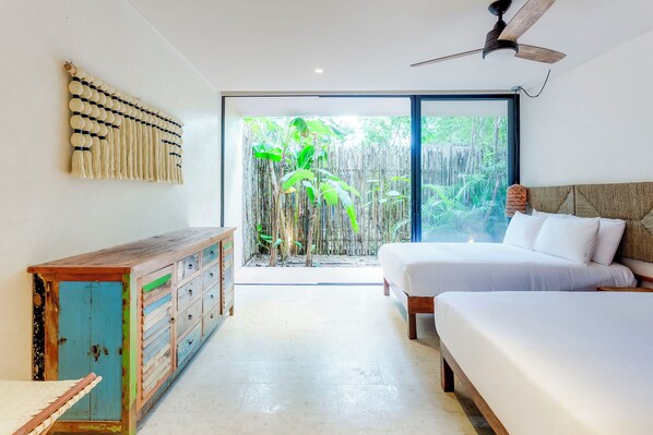 A modern bedroom with a large window, a ceiling fan, and a wooden dresser. - Gorgeous Flowy Space with Wrap-around Private Pool (Tulum)
