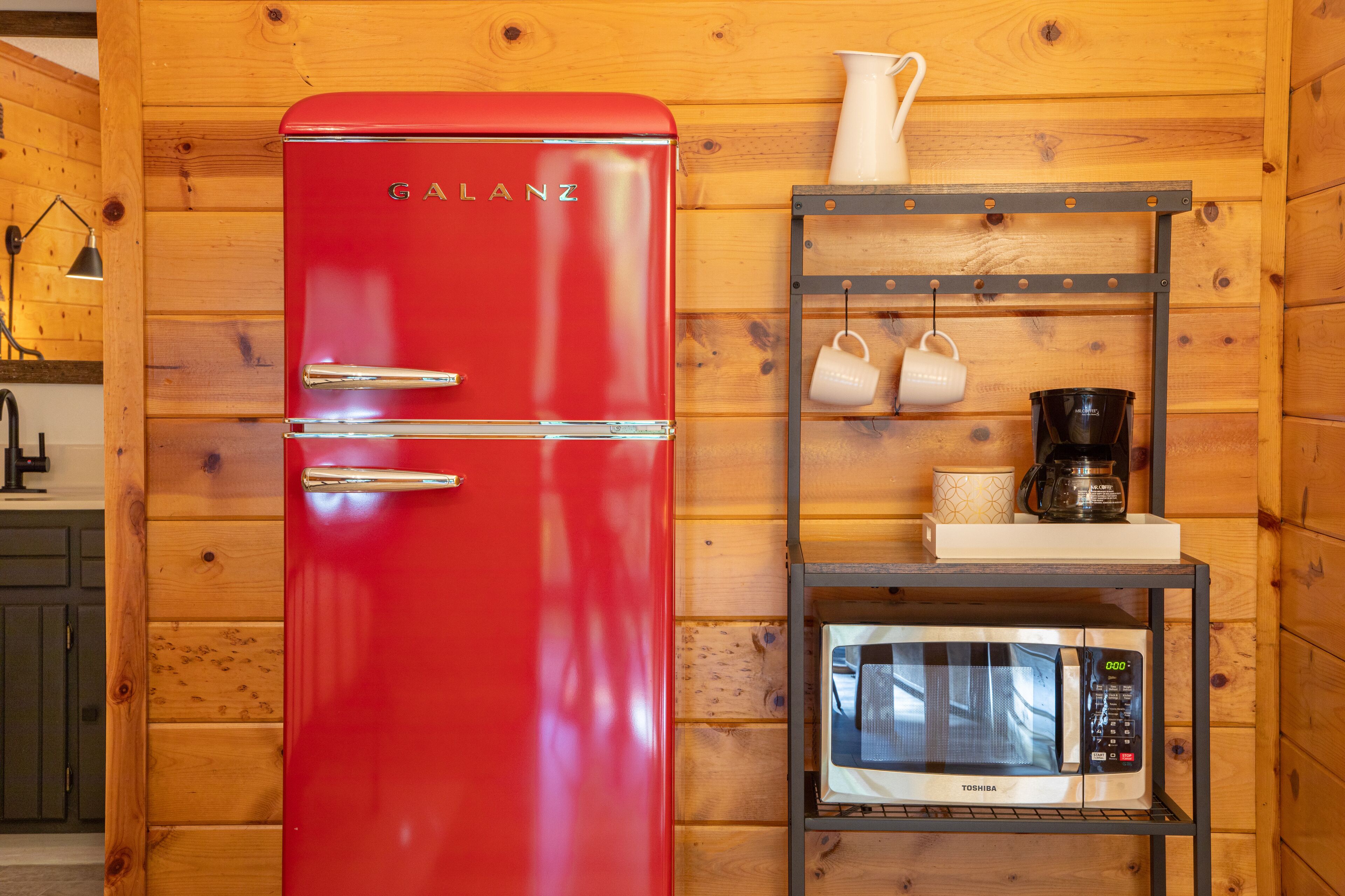 A red Galanz refrigerator, a white microwave, and a shelf with a coffee maker and cups.