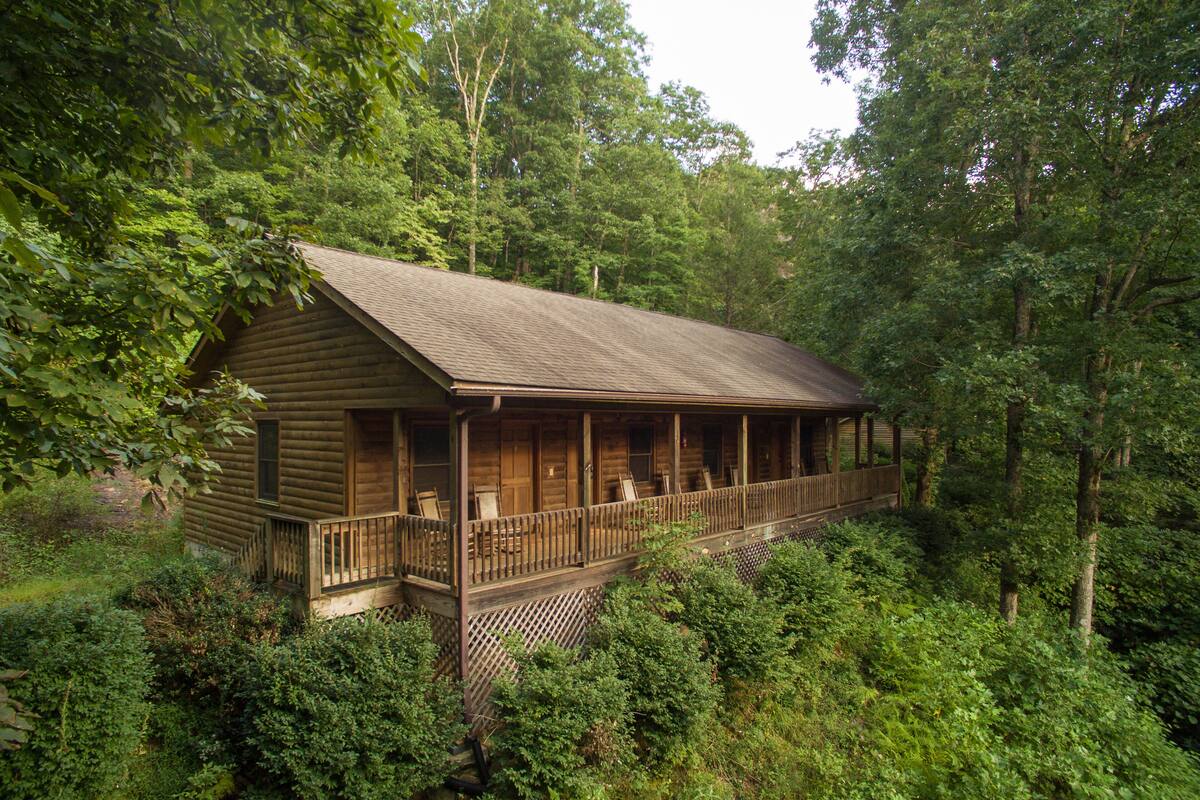 Eine Blockhütte mit Veranda und mehreren Fenstern, umgeben von dichtem Wald.