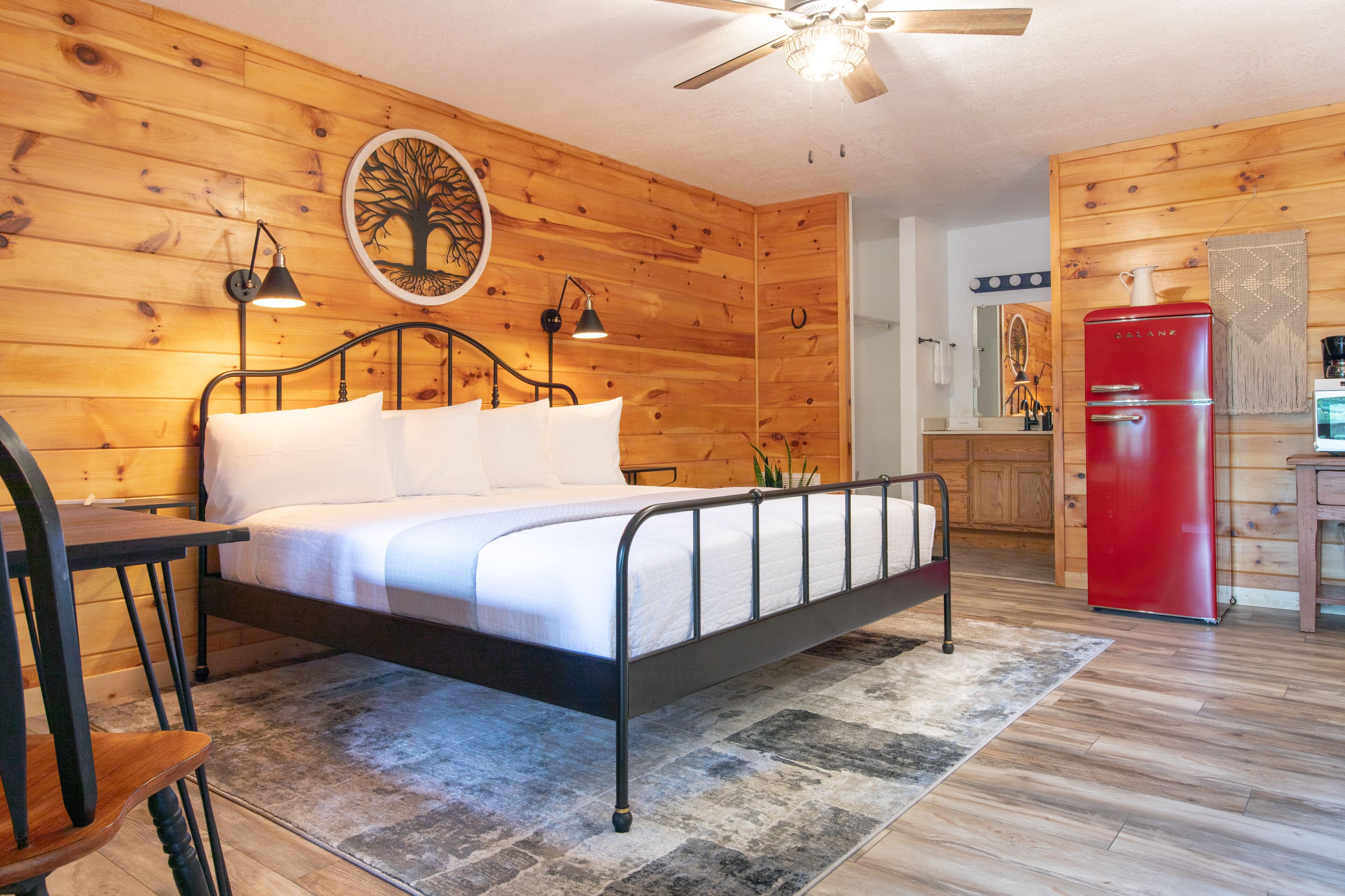 A wooden-paneled bedroom with a bed, bedside lamps, and a ceiling fan.