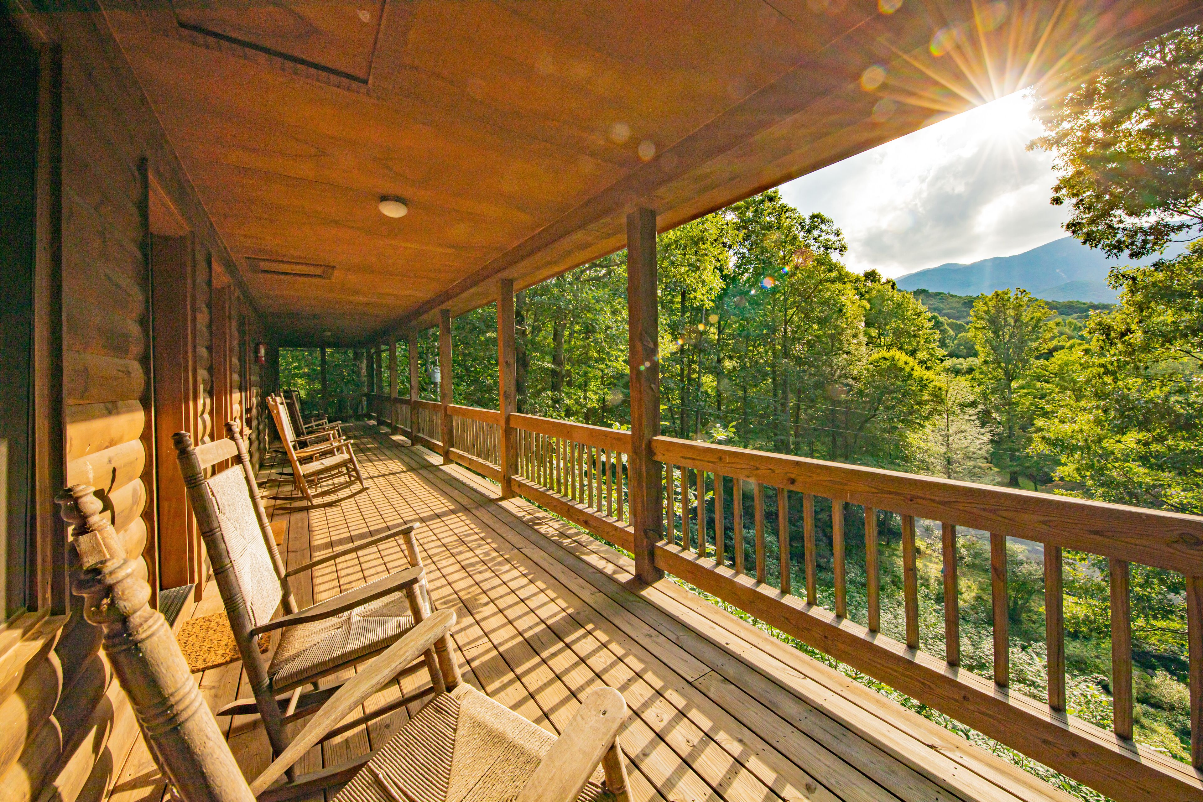 Une terrasse en bois, avec des chaises en bois et une balustrade donnant sur un paysage boisé.