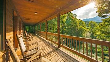 Une terrasse en bois, avec des chaises en bois et une balustrade donnant sur un paysage boisé.
