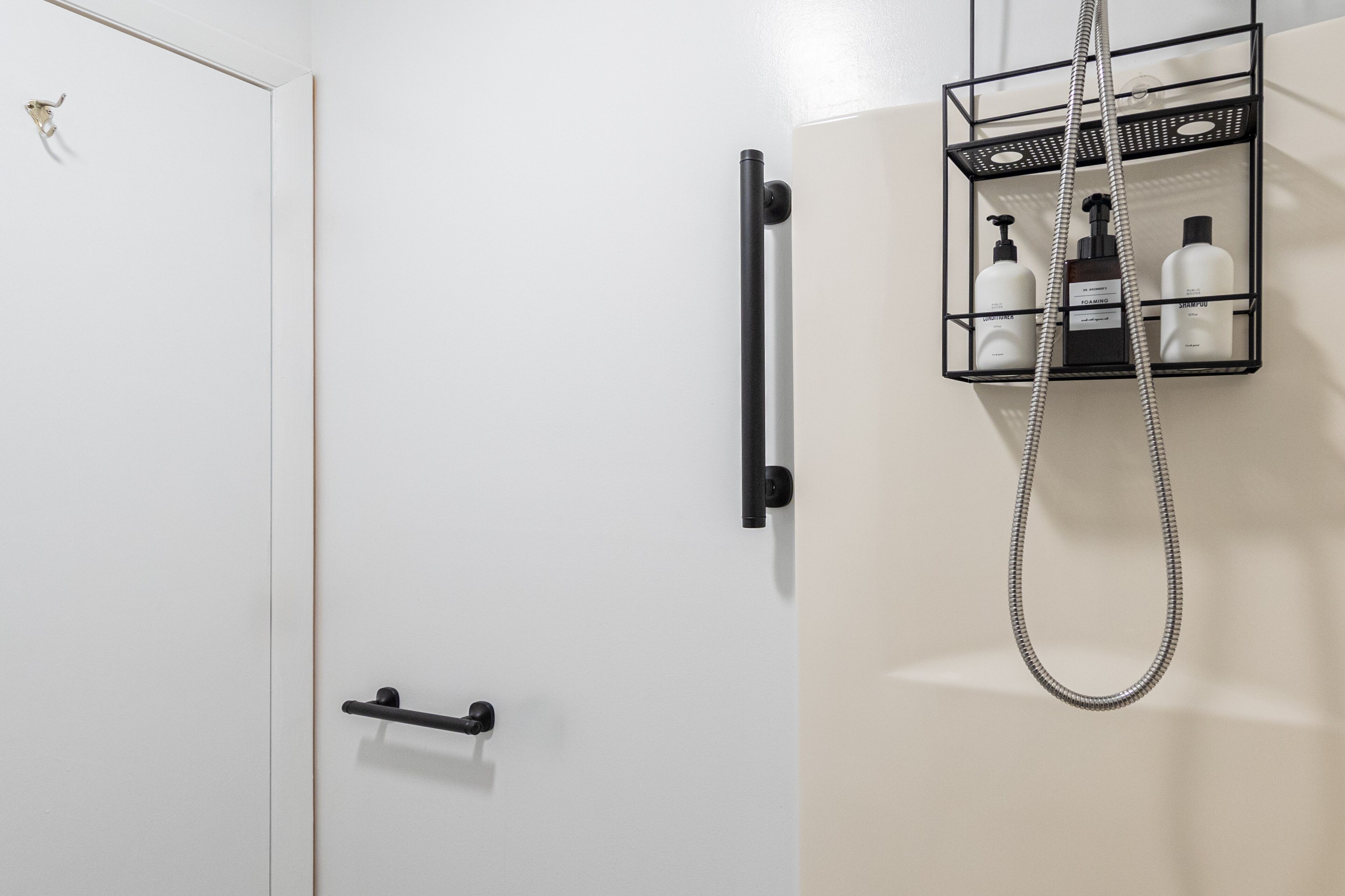 Un bagno con una porta bianca, un porta asciugamani nero e una doccia con cornice nera e soffione argentato.