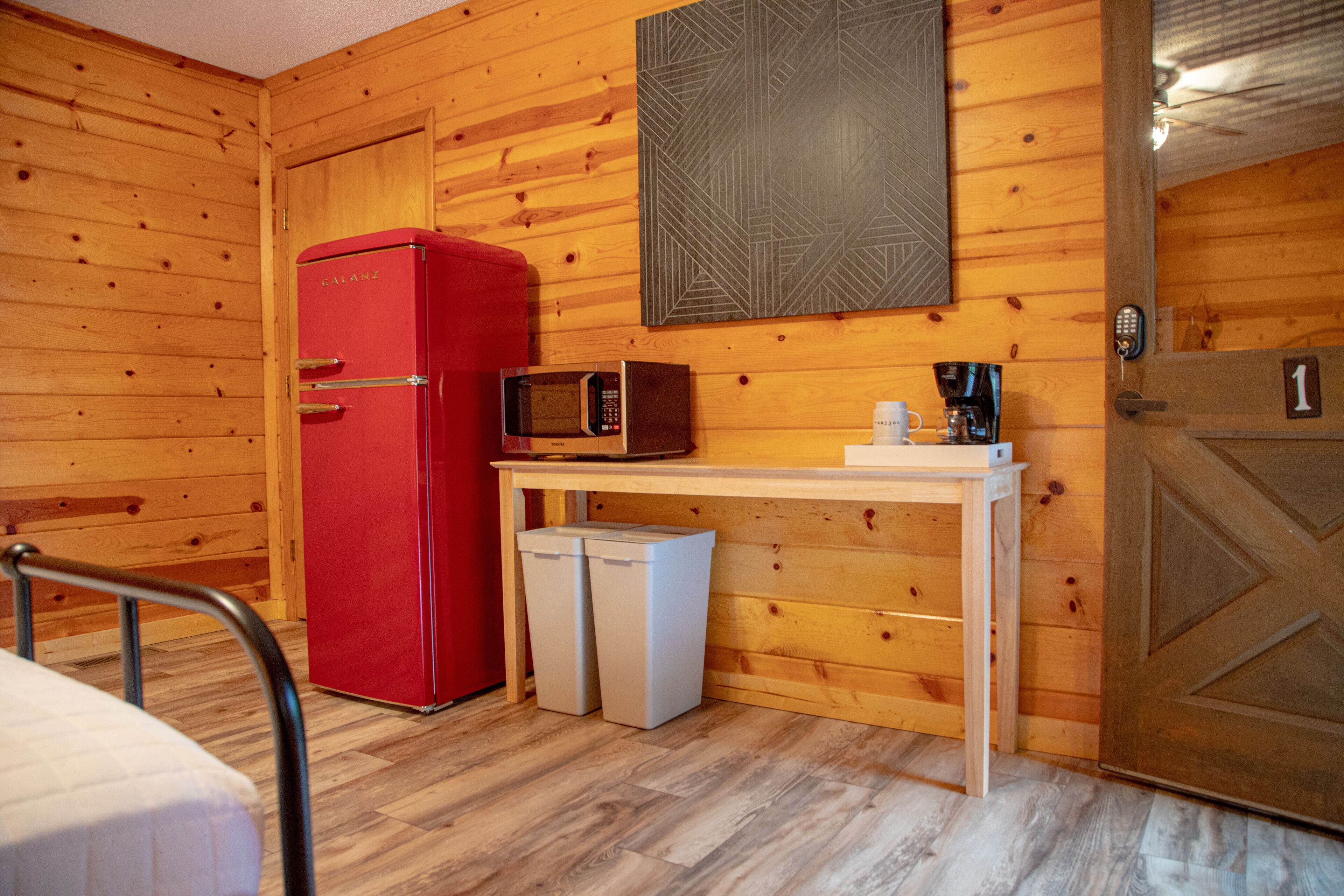 A compact room with a wooden interior, a red refrigerator, a microwave, a small table with a coffee maker, and a door marked with the number 1.