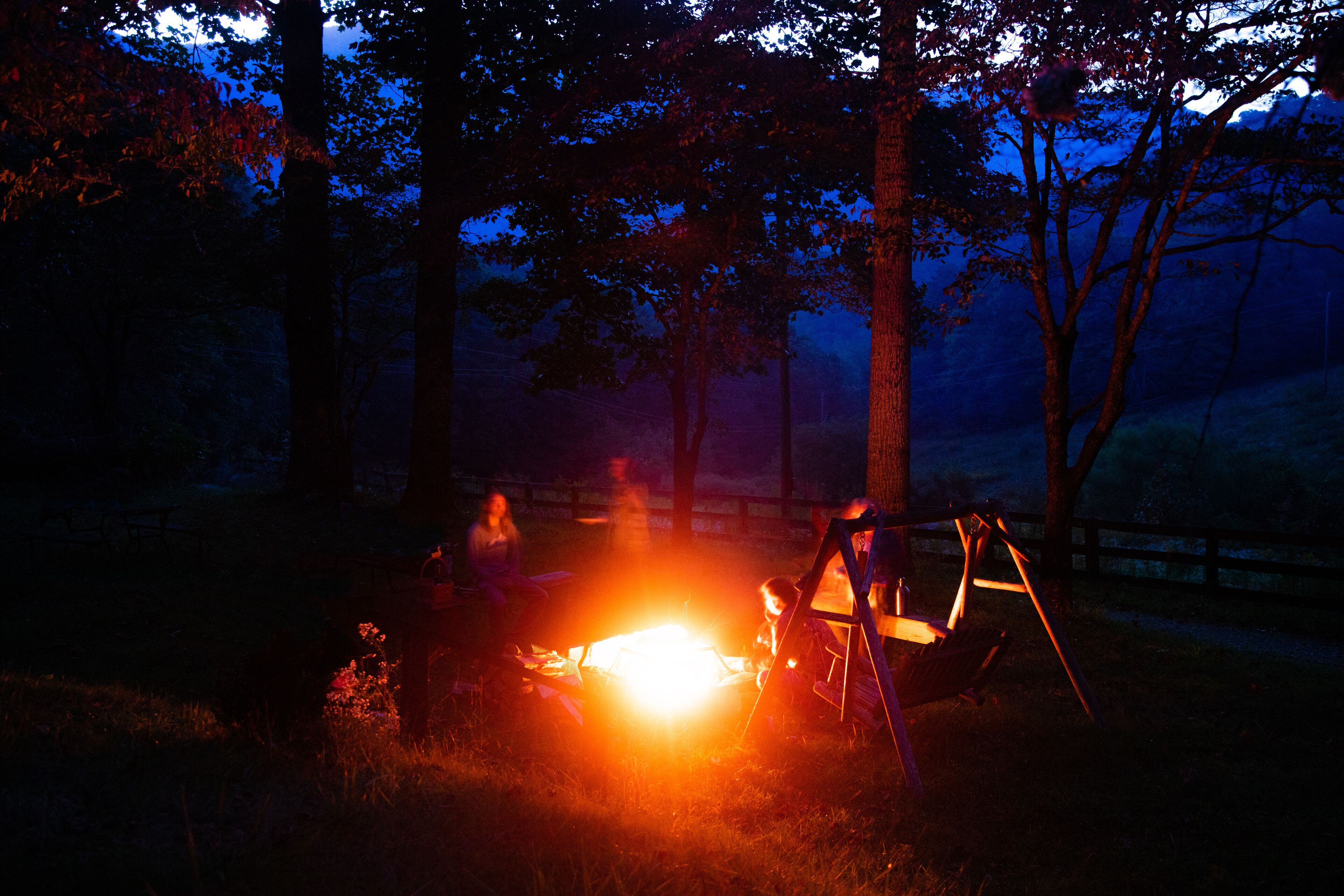 A campfire with a swing set in a wooded area at night.