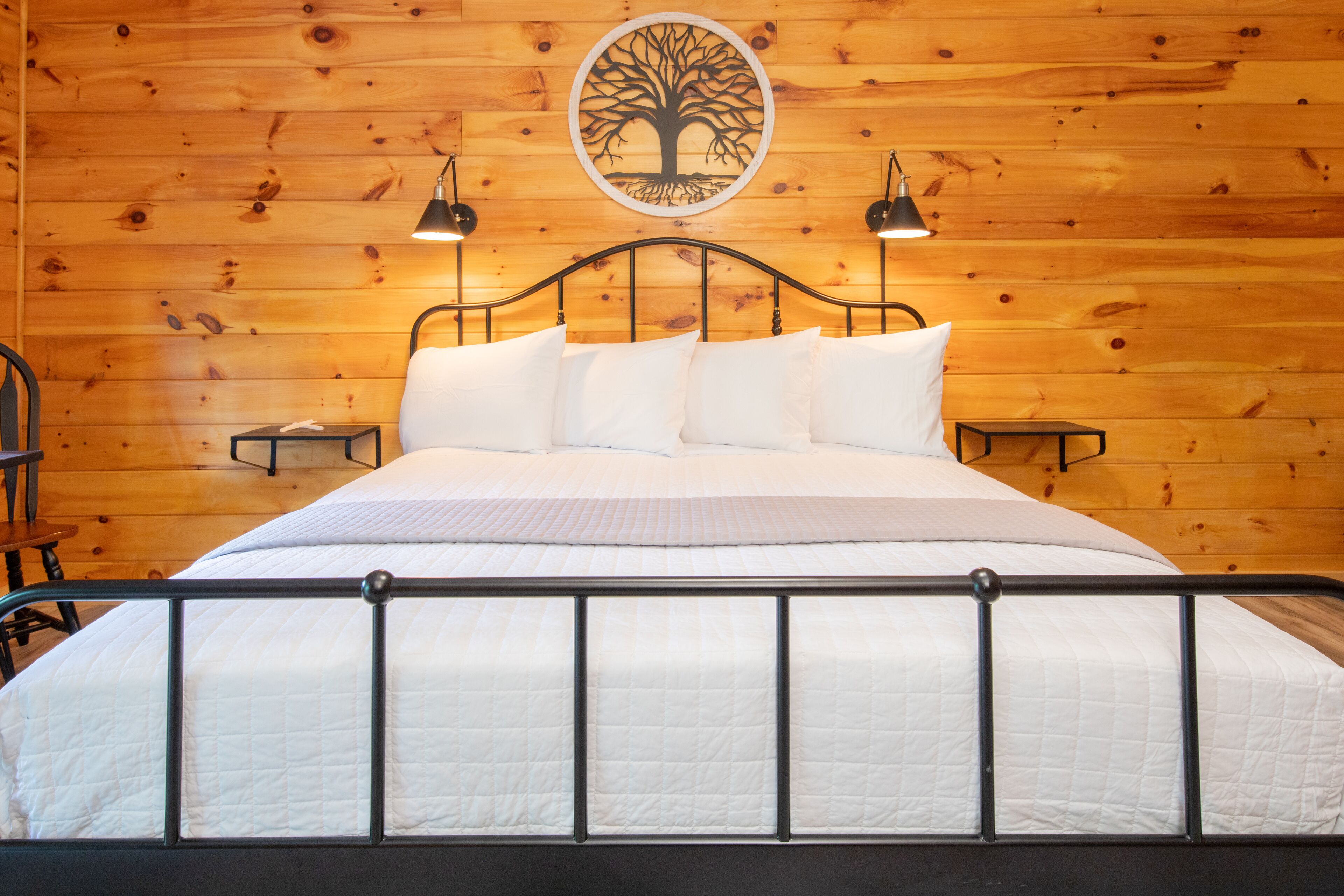 A wooden-paneled room with a bed, two wall-mounted lamps, and a circular wall art piece.