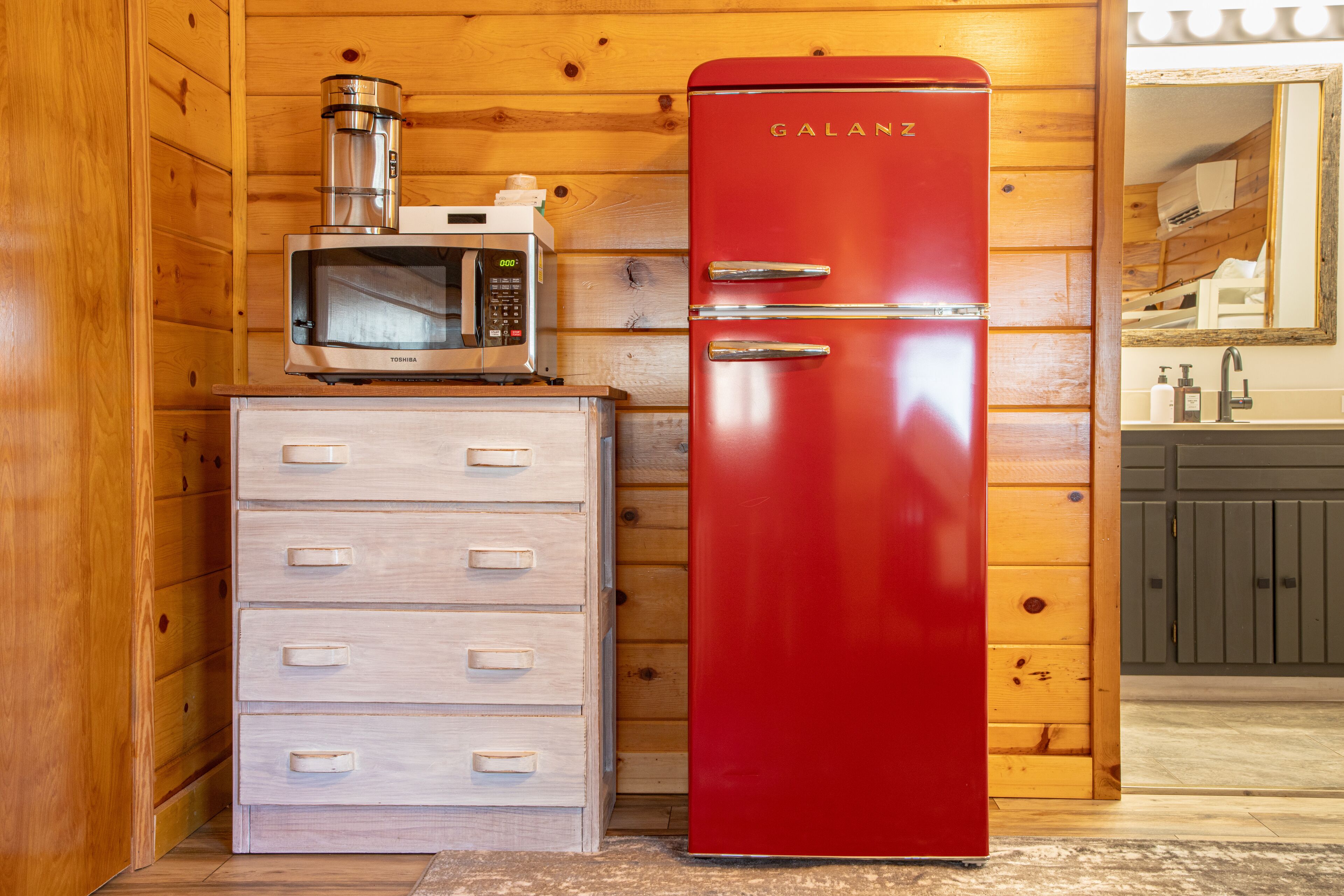 Een compacte keuken met een rode Galanz koelkast, een magnetron en een houten kastje met lades.