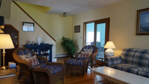 A living room with wicker furniture, a sofa, and a table. There is a staircase in the background. - Short Sands View - Spacious Beach Home, Sleeps 18, Easy Walk to Short Sands Beach (York)