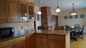 A kitchen with wooden cabinets, a granite countertop, a brick fireplace, and pendant lighting. - Short Sands View - Spacious Beach Home, Sleeps 18, Easy Walk to Short Sands Beach (York)