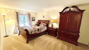 Une chambre à coucher comprenant un lit, une table de chevet, une commode, une lampe et une fenêtre avec des rideaux.