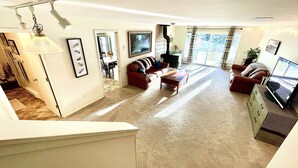 Un salon spacieux doté d’un grand téléviseur, de sièges confortables et offrant une vue sur l’extérieur grâce à de grandes fenêtres.