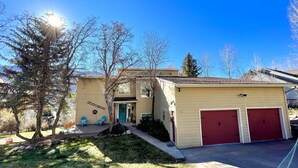 Une maison à deux étages avec un garage, une véranda à l’avant dotée de chaises bleues et un ciel d’un bleu éclatant.