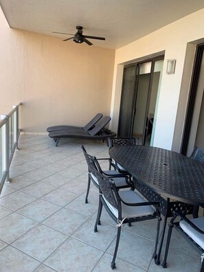 A covered patio with a round metal table and chairs, a ceiling fan, and two lounge chairs.