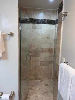 Une douche entièrementClose avec des carreaux beiges et un bord en marbre noir.