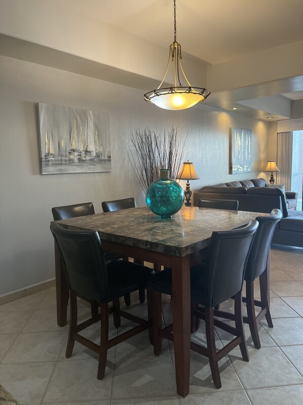 Un coin repas avec une table en marbre, des chaises noires, un vase turquoise et un tableau représentant des voiliers.