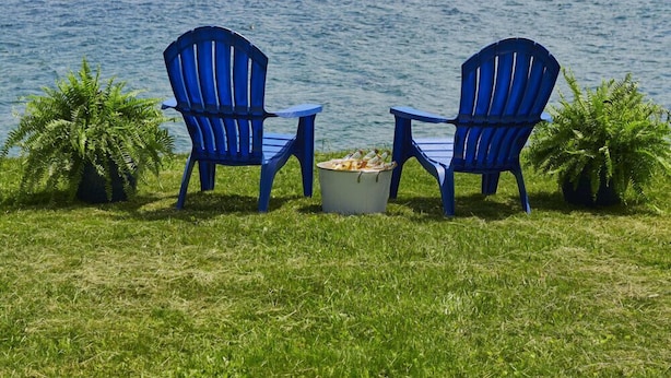 Two blue Adirondack chairs facing a lake with a grassy area in the foreground and a forested hill in the background. - Mint Private Lakefront Skaneateles, 4BR/2 Bath w/50ft Lake Frontage w/Dock (Skaneateles)