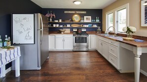 A kitchen with white cabinets, a stainless steel refrigerator, a wooden countertop, and a sign that reads "Welcome to The Hake!" - Mint Private Lakefront Skaneateles, 4BR/2 Bath w/50ft Lake Frontage w/Dock (Skaneateles)