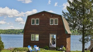 A wooden cabin with a large window and a door, situated by a lake. - Mint Private Lakefront Skaneateles, 4BR/2 Bath w/50ft Lake Frontage w/Dock (Skaneateles)