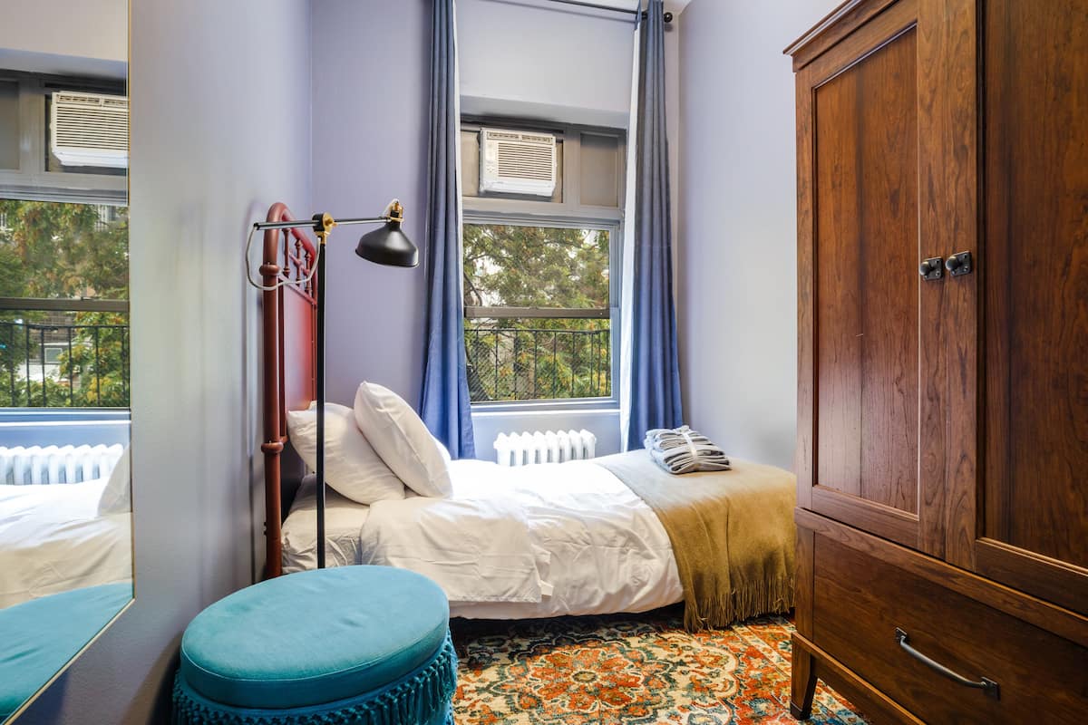 A bedroom with a bed, a wardrobe, a window with curtains, and a radiator.