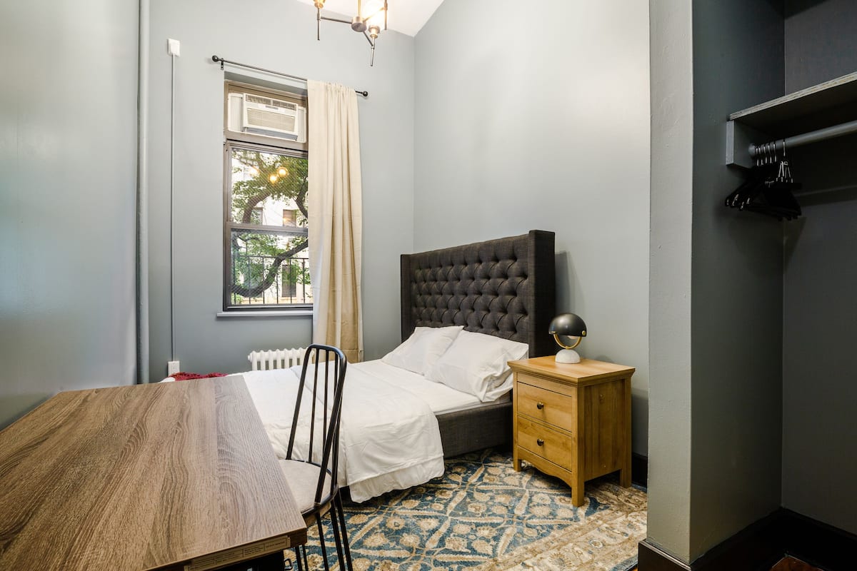 A bedroom with a bed, bedside table, chair, and a window with curtains.