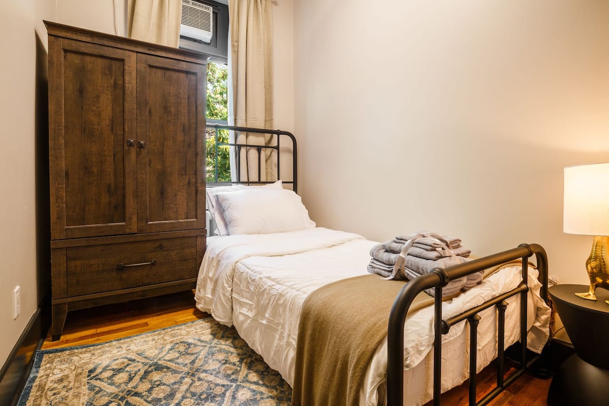 A bedroom with a bed, a wardrobe, a window, a lamp, and a rug.