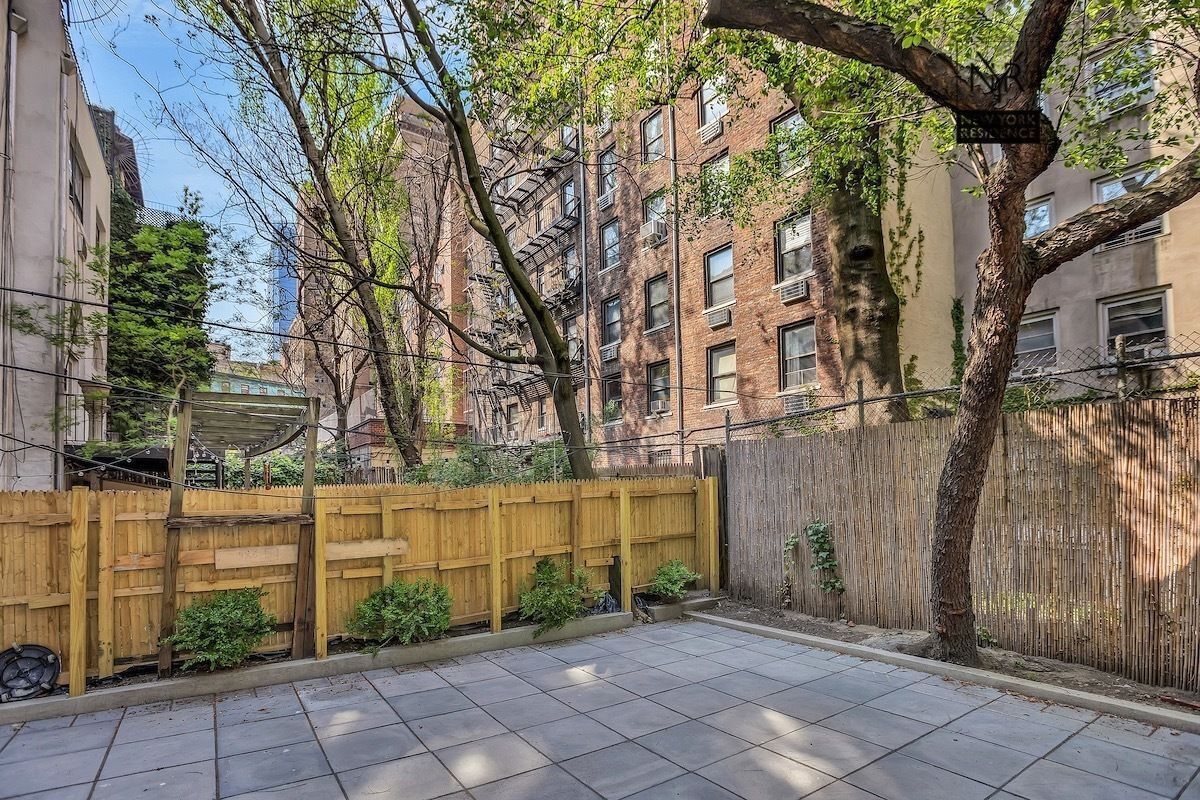 A courtyard with a tiled floor, a wooden fence, and a tree.