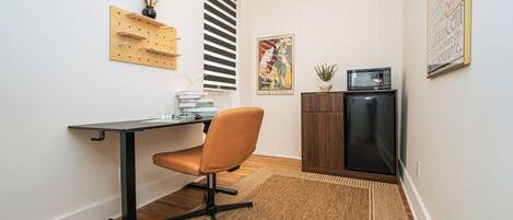 A compact office space with a desk, chair, pegboard, radiator, and a small cabinet.