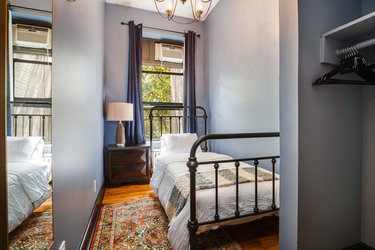 A bedroom with two beds, a nightstand with a lamp, and a window with curtains.
