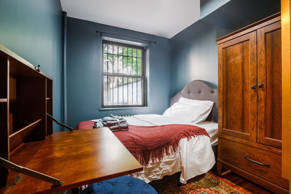A bedroom with a bed, a wooden wardrobe, a window, and a table.