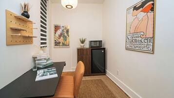 A dining area with a table, chairs, a wall-mounted shelf, a small cabinet, and a poster.
