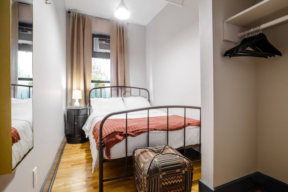 A bedroom with a bed, bedside table, lamp, and a hanging closet rod.
