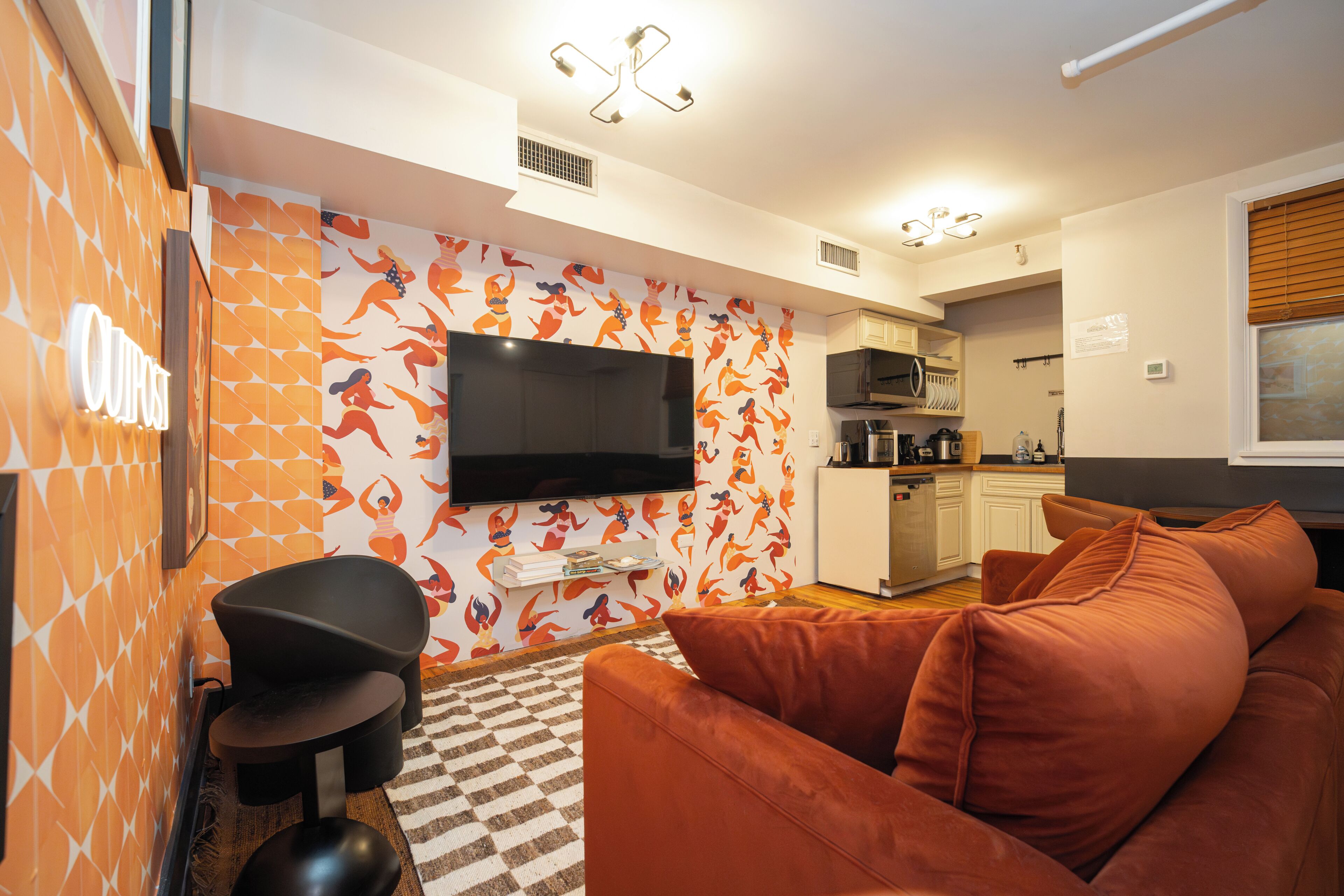 Ein modernes Wohnzimmer mit einer Couch, einem flachbildfernseher an der Wand und einer Küchenzeile im Hintergrund.