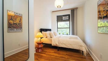 A bedroom with a bed, a bedside lamp, a window with curtains, and a poster on the wall.
