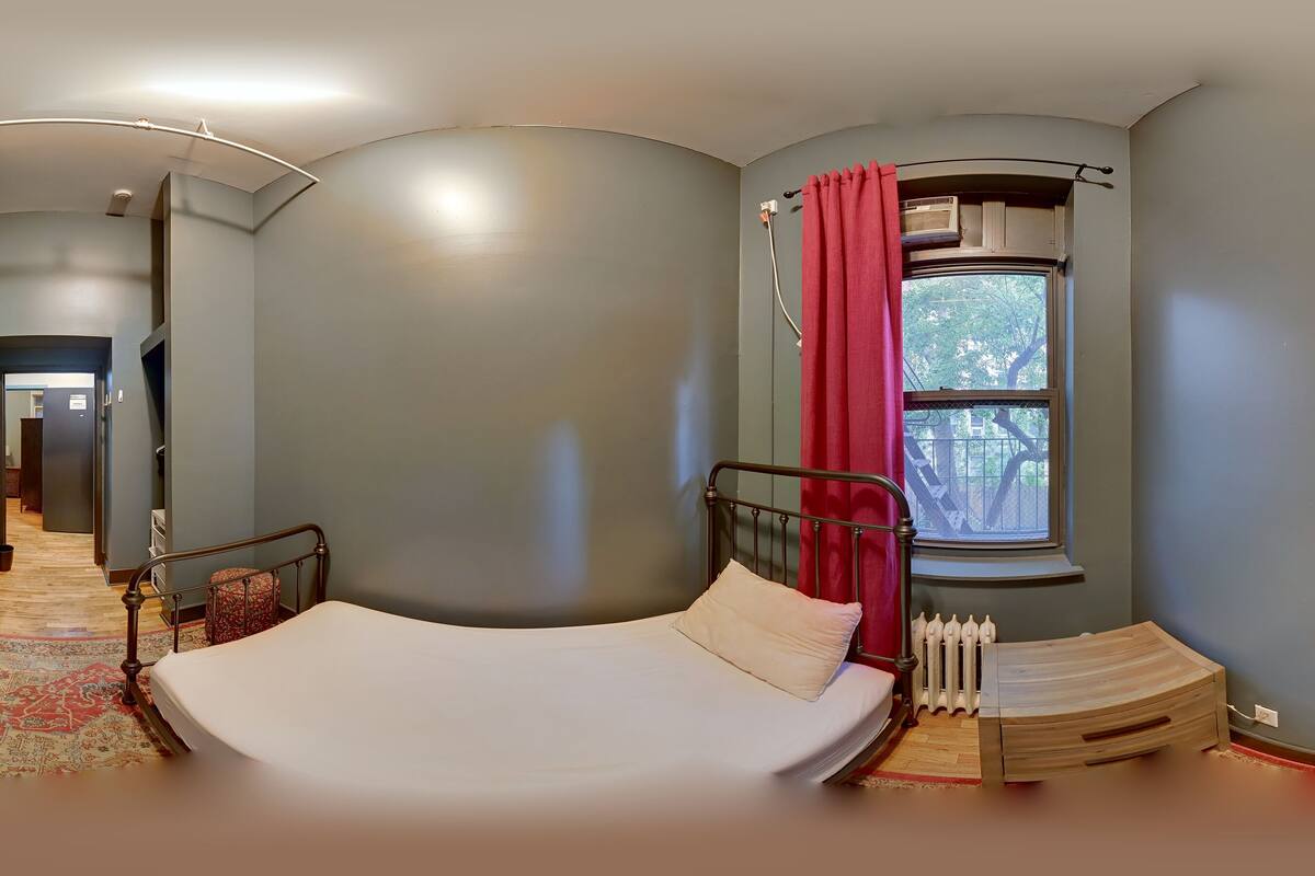 A room with a bed, a window with a red curtain, a radiator, and a curved ceiling.