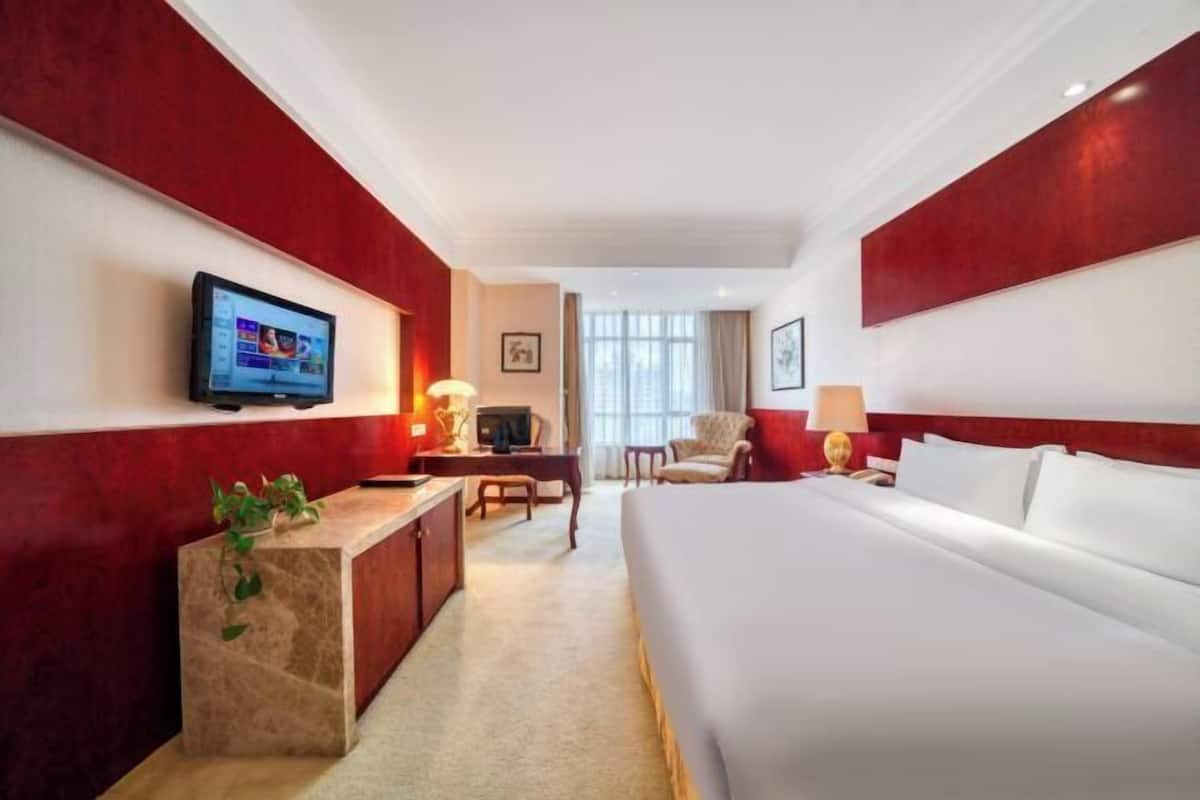 Une chambre d’hôtel avec un grand lit, un bureau, une télévision et un mur d’accent de couleur rouge.
