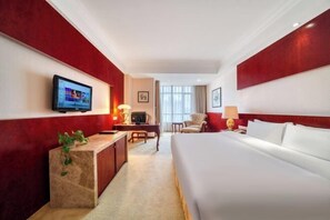 Een hotelkamer met een groot bed, een bureau, een televisie en een rode accentmuur.