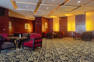 Un vestíbulo de hotel con áreas de descanso, mesas y una alfombra estampada.