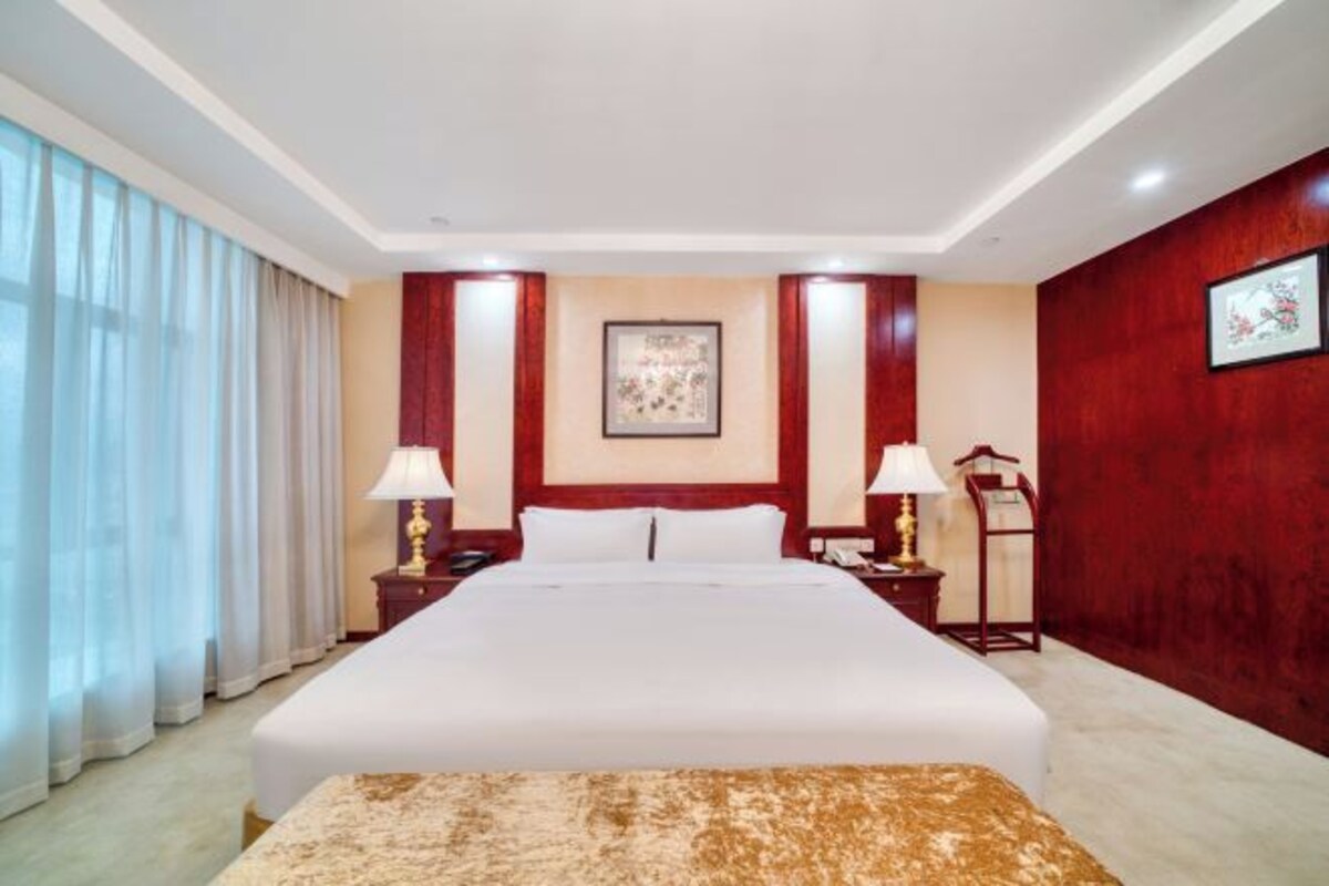 Hotelkamer met een groot bed, twee nachtkastjes met lampen, een kunstwerk in een lijst aan de muur, en een rode accentmuur.