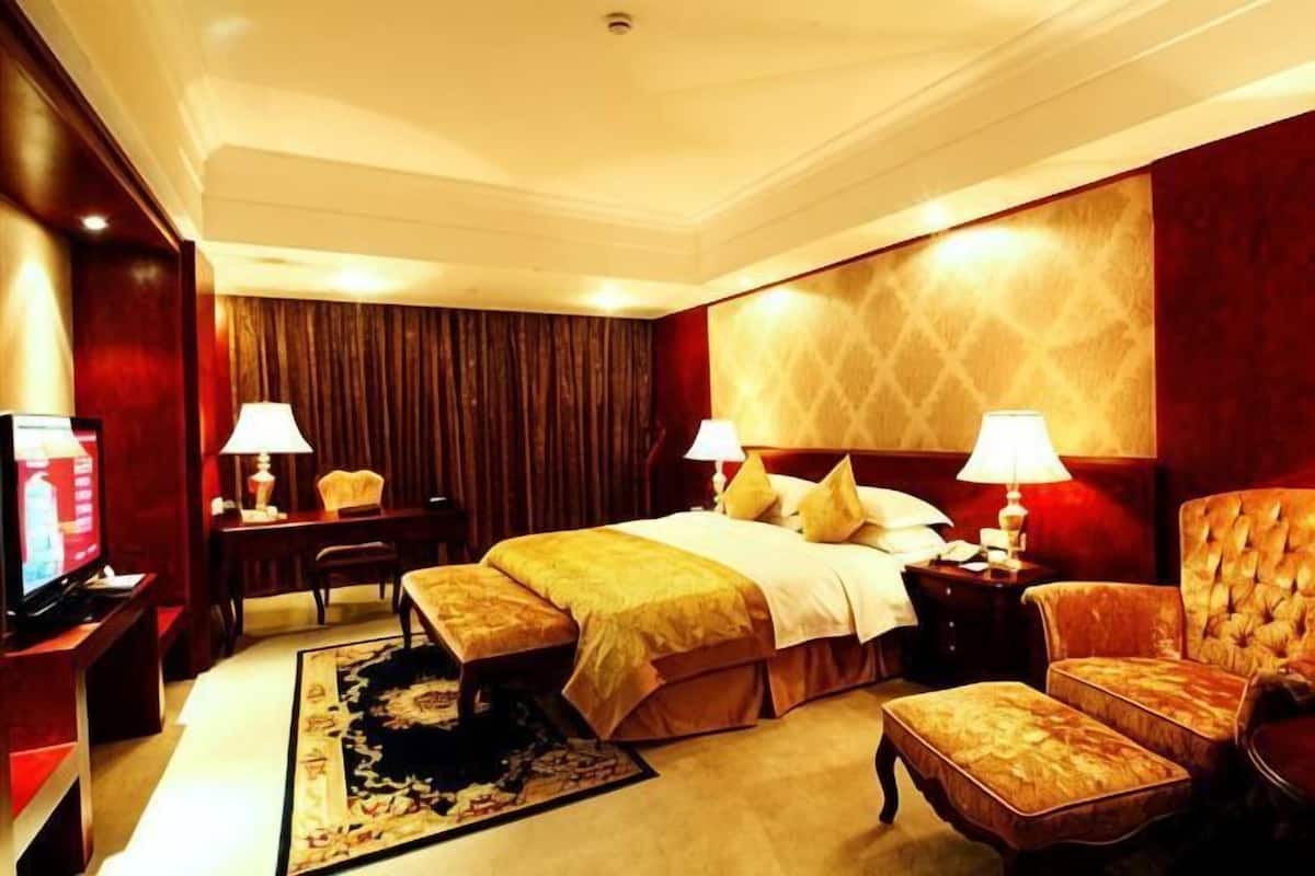 Une chambre d’hôtel avec un grand lit, deux tables de chevet avec des lampes, une télévision, un canapé et un sol recouvert de moquette.
