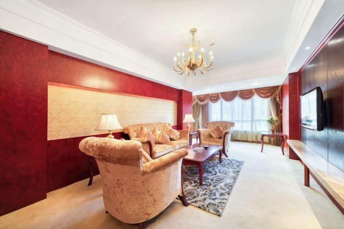 Un salon spacieux avec un mur d’accent rouge, un lustre et un téléviseur à écran plat.