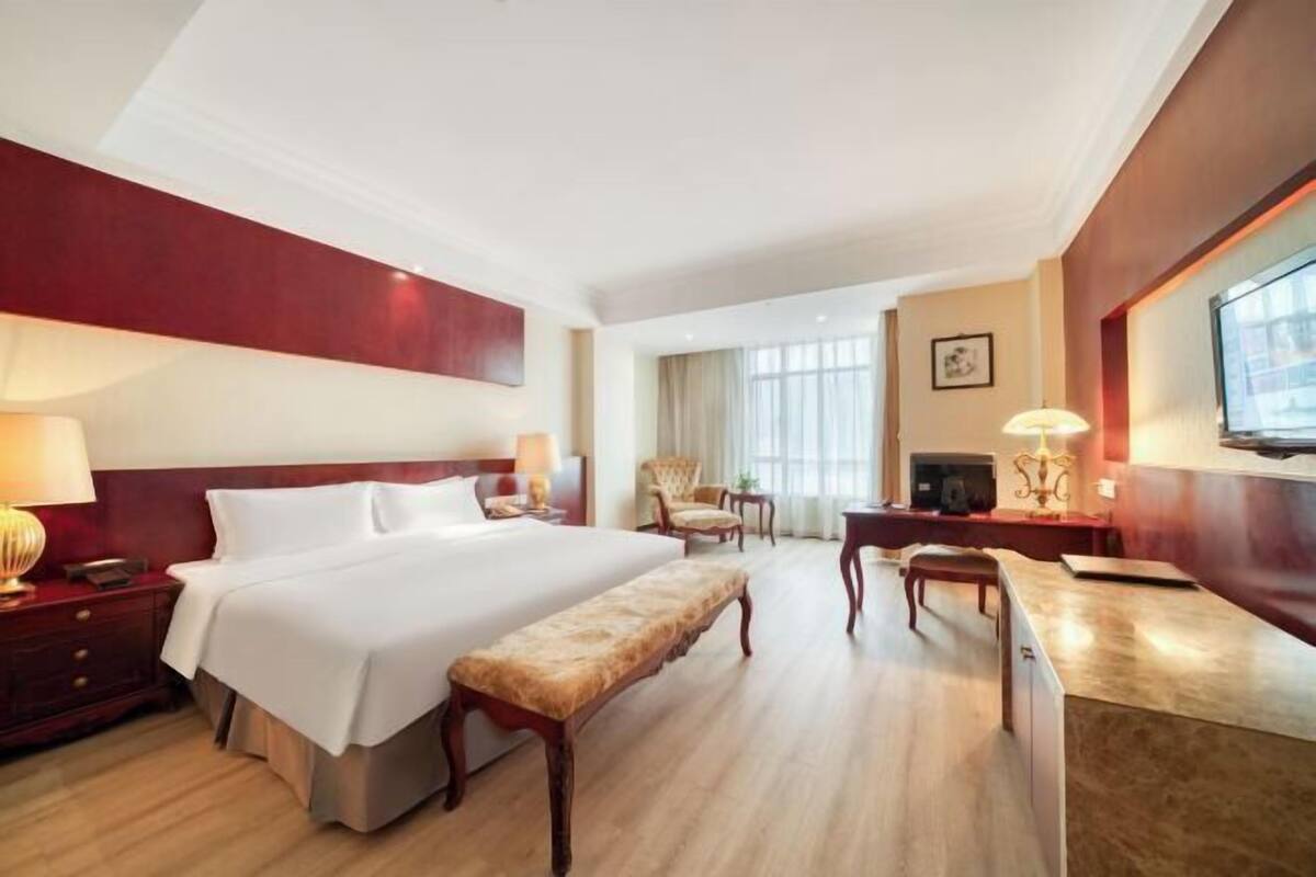 Une chambre d’hôtel avec un grand lit, un bureau, une chaise, un banc et un téléviseur.