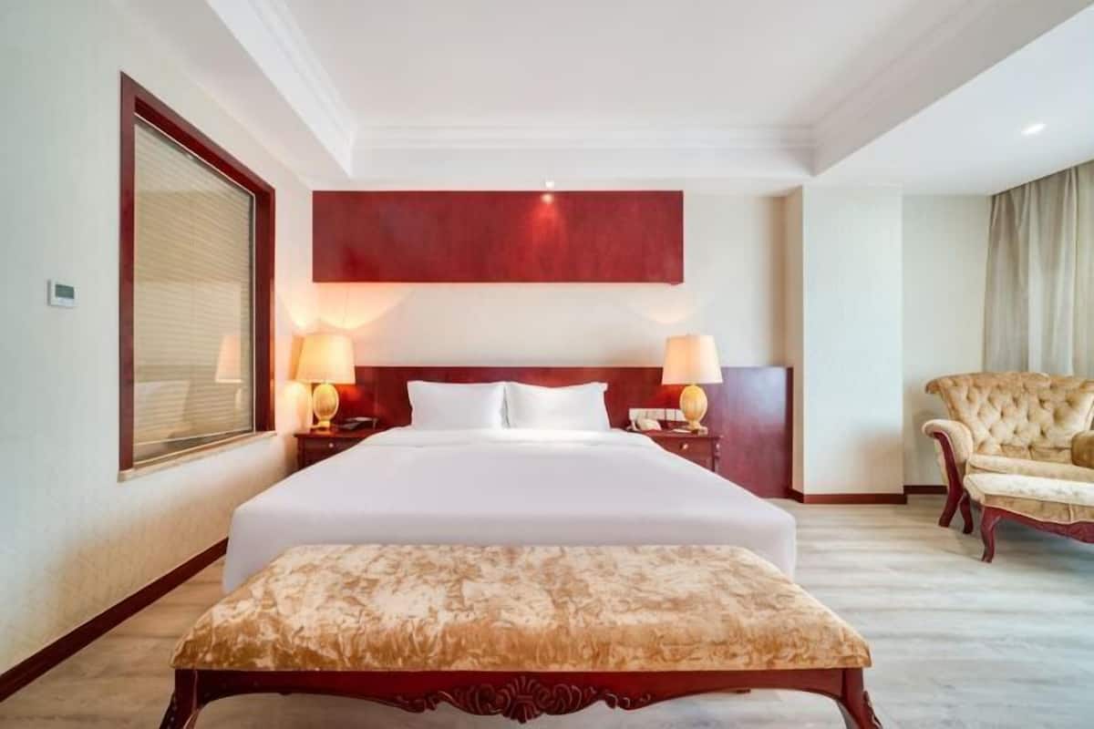 Une chambre d’hôtel avec un grand lit, deux tables de chevet avec des lampes, une chaise et un mur d’accent rouge.