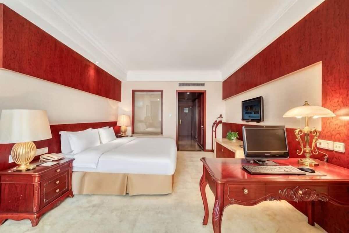 Une chambre d’hôtel équipée d’un lit, d’un bureau, d’une lampe, d’une télévision et d’une porte donnant sur une autre pièce.