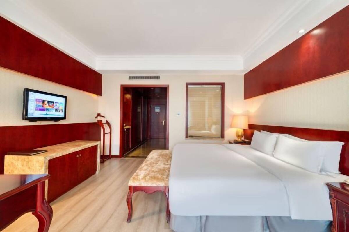 Une chambre d’hôtel avec un grand lit, un bureau avec un ordinateur, un banc et un téléviseur fixé au mur.