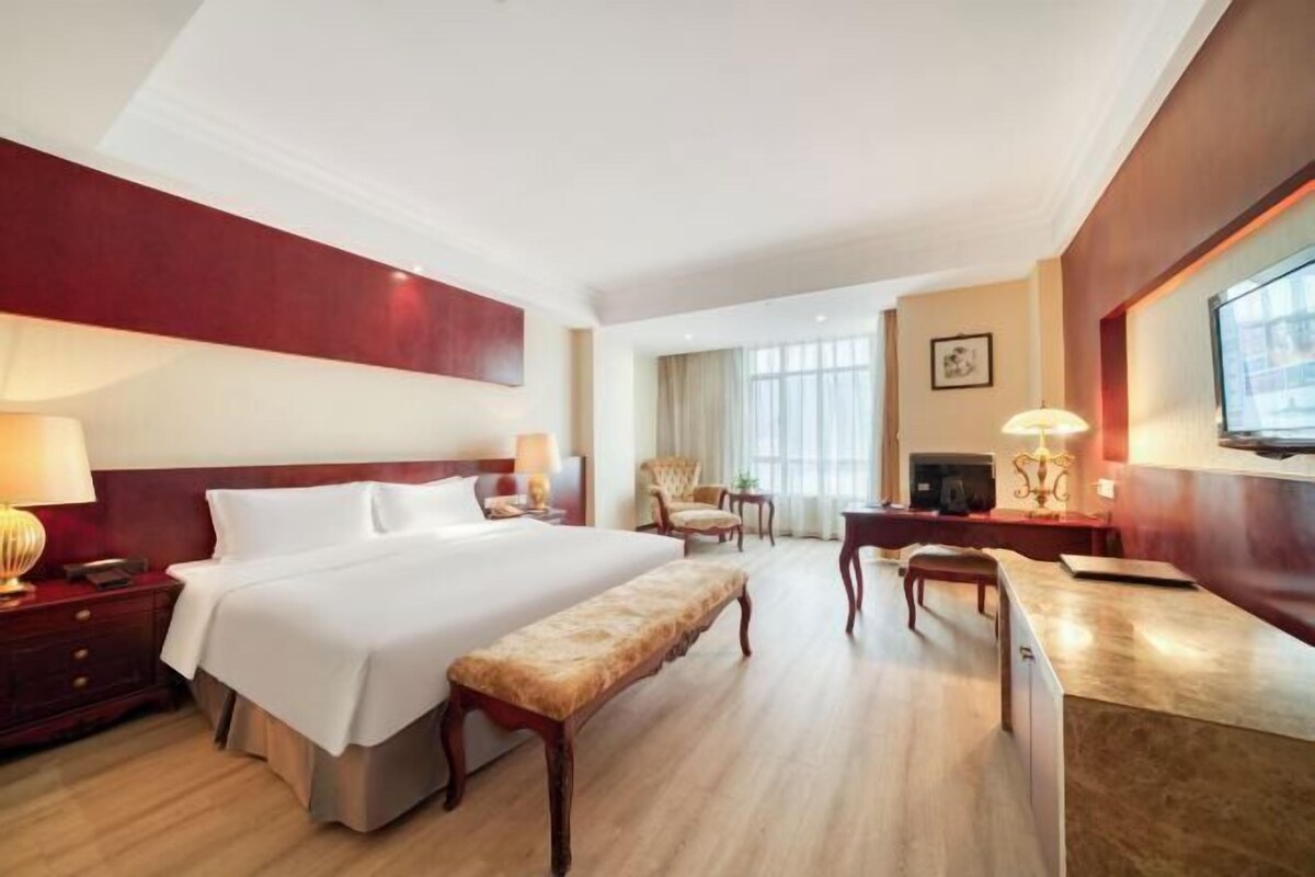 Een hotelkamer met een groot bed, een bureau, een stoel, een bankje en een televisie.