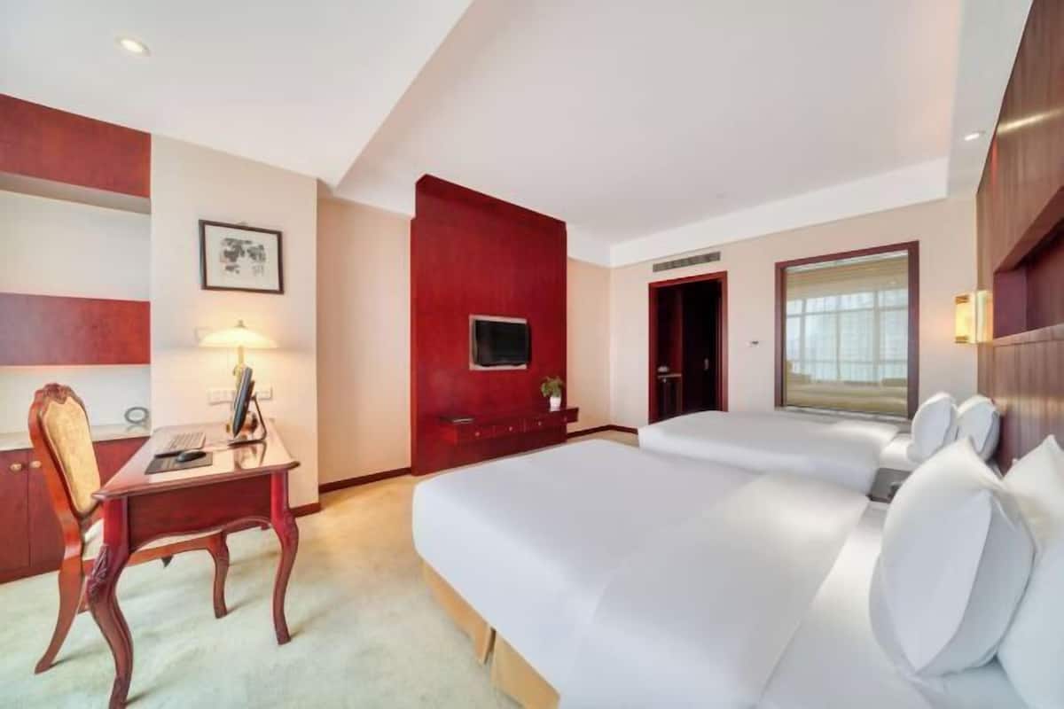 Une chambre d’hôtel avec un bureau, deux lits, une télévision et une fenêtre.