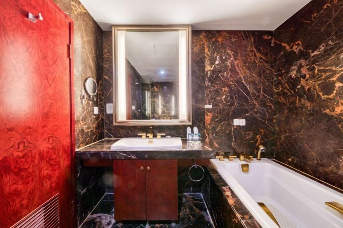 Een badkamer met een marmeren wastafelmeubel, een grote spiegel, een badkuip en een rode deur.